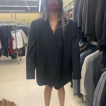 Savers - friend stunnin!!!! - A woman in a black pinstripe blazer and matching shorts, with glasses and a red face mask, stands in a clothing store aisle with racks of suits and casual wear. - Thrift Stores Near Me - Medford, New York