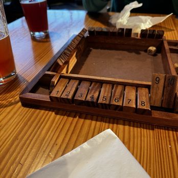 Eastern Divide - Games - A tabletop scene with a wooden board game, drinks, and a person reaching over, in a casual dining setting. - Brewpubs Near Me - Blacksburg, Virginia