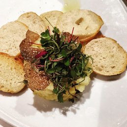 Chilean Sea Bass - A plate featuring Chilean sea bass topped with microgreens, accompanied by slices of toasted bread, served on a white dish.