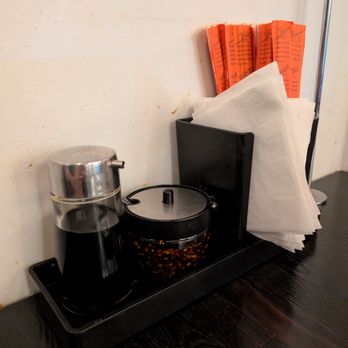 Dumpling Cafe - A condiment station on a black tray includes soy sauce, chili flakes, napkins, and chopsticks in a restaurant setting. - Dim Sum Near Me - Santa Fe, New Mexico
