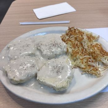 Kettle Restaurant - 2 Biscuits and Gravy with Hashbrowns - A plate with biscuits covered in white gravy and topped with black pepper, served alongside crispy hashbrowns, on a wooden table at a casual restaurant. - Breakfast & Brunch Near Me - Tucson, Arizona