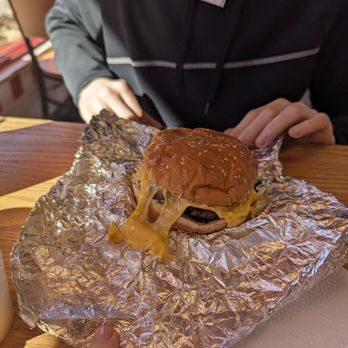 Five Guys - a man sitting at a table with a hamburger - Burgers Near Me - Enfield, Connecticut