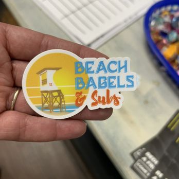 Beach Bagels & Subs - a person holding a beach bagels sticker - Juice Bars & Smoothies Near Me - Wilmington, North Carolina Beach Bagels & Subs - a person holding a beach bagels sticker - Juice Bars & Smoothies Near Me - Wilmington, North Carolina