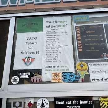 Vegan Vato - Vegan fun facts and half of the menu - The image shows a menu board at Vegan Vato in Albuquerque, NM, featuring vegan protein sources such as beans, seeds, and grains, with their respective weights. The board also displays prices for T-shirts and stickers, and includes various stickers and decals at the bottom, some promoting veganism and local organizations. The menu emphasizes plant-based protein options and community involvement. - Food Trucks Near Me - Albuquerque, New Mexico