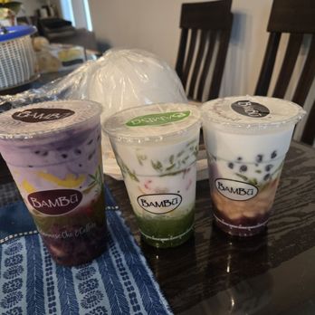 BAMBU - Our desserts - Three cups of bubble tea with different flavors and toppings are placed on a dark table, with a blue patterned cloth nearby. - Bubble Tea Near Me - Minneapolis, Minnesota