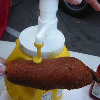 Uncle Bill's Gourmet Corn Dogs - a hot dog being dipped with mustard - Hot Dogs Near Me Uncle Bill's Gourmet Corn Dogs - a hot dog being dipped with mustard - Hot Dogs Near Me