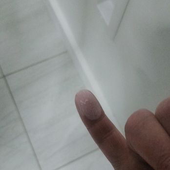 Ana's Cleaning Services - The image shows a person's hand with the middle finger extended, pointing towards a wall. The wall has a small, square opening or vent near the floor. The floor is tiled with light-colored tiles, and the setting appears to be indoors, possibly in a bathroom or utility room. - Home Cleaning Near Me - Durham, North Carolina