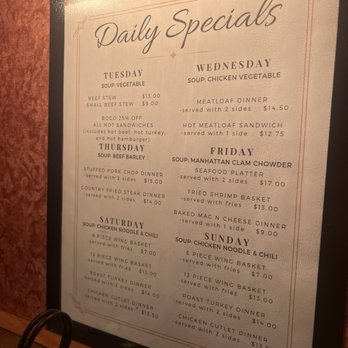 Maple Restaurant - A printed menu board titled 'Daily Specials' lists meal options for Tuesday through Sunday, including soups, sandwiches, and dinners. Each day features specific dishes such as beef stew, chicken vegetable soup, and seafood platters, with prices and descriptions. The board is framed and placed on a wooden surface, with a warm, inviting background. - New American Near Me - Ambridge, Pennsylvania