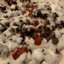 Mild - The image shows a dish topped with a generous amount of white sauce, ground meat, and small dollops of red sauce, served on a plate. The dish appears to be a savory meal, possibly a type of Mexican or Middle Eastern cuisine, with a focus on the toppings and sauces.
