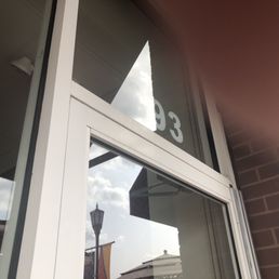 number  above door - The image shows a close-up of a storefront window with white framing, reflecting the sky, clouds, and a streetlamp outside. Part of the business signage is visible at the top of the window, with the number '3' and other characters partially seen. The exterior wall is made of brick, and the photo is taken at an upward angle, capturing the reflection and architectural details.