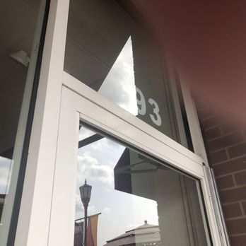 Gong Cha - Plainview - number  above door - The image shows a close-up of a storefront window with white framing, reflecting the sky, clouds, and a streetlamp outside. Part of the business signage is visible at the top of the window, with the number '3' and other characters partially seen. The exterior wall is made of brick, and the photo is taken at an upward angle, capturing the reflection and architectural details. - Bubble Tea Near Me - Plainview, New York