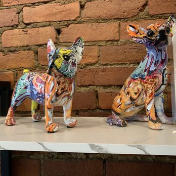 Hound and Mare - Decor - Two painted animal figurines, a dog and a cat, sit on a white marble shelf with a brick wall background, showcasing vibrant, abstract patterns. - Cafes Near Me - Ithaca, New York