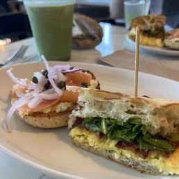 Half of the smoked salmon bagel sandwich and half of the breakfast sandwich on ciabatta with bacon, with matcha iced latte. Half of the smoked salmon bagel sandwich and half of the breakfast sandwich on ciabatta with bacon, with matcha iced latte.