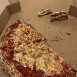 Half of a crab/chicken cheese pizza. Heaven in a pie - A slice of pizza with chicken, cheese, and tomato sauce in a cardboard pizza box, with some crust pieces and crumbs around.