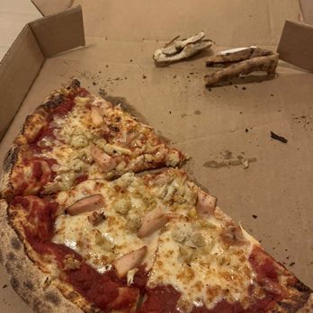 Idiom Brewing - Half of a crab/chicken cheese pizza. Heaven in a pie - A slice of pizza with chicken, cheese, and tomato sauce in a cardboard pizza box, with some crust pieces and crumbs around. - Breweries Near Me - Frederick, Maryland