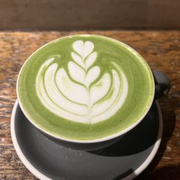 Matcha latte - A green matcha latte with white latte art in a black cup on a wooden table, photographed from above.