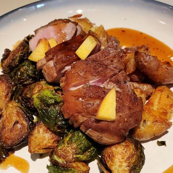 NoJa - Duck Breast - A dish featuring roasted meat, Brussels sprouts, and potatoes, garnished with small yellow pieces, served with a sauce. - New American Near Me - Mobile, Alabama
