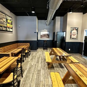 Chaps Pit Beef - The image shows the interior of Chaps Pit Beef, a Baltimore-style BBQ restaurant. It includes wooden tables and benches arranged along the walls, with additional tables in the center. The walls are decorated with framed pictures and a large sign displaying the restaurant's name and offerings. The ceiling has exposed ductwork, and the flooring is wood-like. The space appears clean and organized, with a mix of seating options and a neutral color palette. - Barbeque Near Me - Baltimore, Maryland