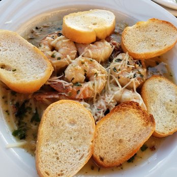 Bugeye Grill - Pesto Shrimp - A plate of shrimp in a creamy, herb-infused sauce is presented with several toasted bread slices arranged around the seafood. The dish appears to be served on a white, round plate, with the shrimp and sauce as the central focus. The bread slices are evenly toasted, providing a crunchy contrast to the tender shrimp and sauce. - Seafood Near Me - Solomons, Maryland