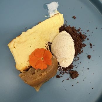 Writer's Room - Adelaide Cheesecake - A dessert presentation on a blue tray includes a slice of cheesecake, a scoop of vanilla ice cream, and a serving of apple compote topped with an orange edible flower. There are also crumbled cookie or biscuit crumbs and a small dollop of cream or sauce, arranged with attention to visual appeal. - American Near Me - Urbana, Illinois