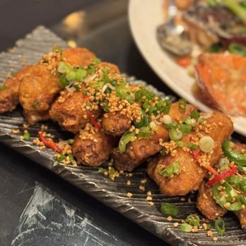 Colette - Chicken wings - Plate of fried chicken wings topped with chopped green onions and crushed peanuts, served on a black textured platter. - Breakfast & Brunch Near Me - Pasadena, California