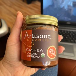 a hand holding a jar of artisana organics cashew spread