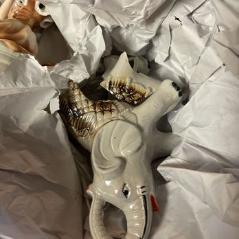 The UPS Store - Broken - A ceramic elephant figurine with painted details, including a red ear and black eyes, is shown with a broken trunk. The figurine is surrounded by crumpled white paper, indicating it may have been packed or stored. The ceramic surface has decorative patterns, and the broken trunk reveals the interior of the figurine. - Shipping Centers Near Me - Prospect, Connecticut