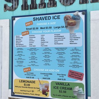 The Shack - Menu - A printed menu board for shaved ice features options for sizes (small, medium, large) with prices, various flavors such as banana, blueberry, cherry, and more, and additional toppings like ice cream, condensed milk, and sour spray. The board includes instructions for choosing flavors and add-ons, with prices for each. It also highlights a lemonade special and vanilla ice cream, with notes on flavor customization and free flavor options. - Shaved Ice Near Me - Macomb, Illinois