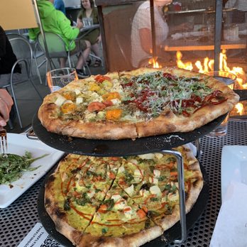 The Flying Goat - two pizzas on a table with a fire in the background - Gastropubs Near Me - Spokane, Washington The Flying Goat - two pizzas on a table with a fire in the background - Gastropubs Near Me - Spokane, Washington