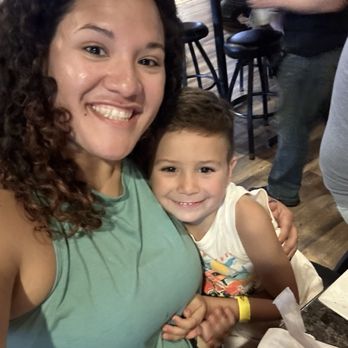 Nutz Deep II - A woman with curly hair and a young boy are smiling for a selfie in a restaurant setting with tables and other patrons in the background. - Burgers Near Me - Marshfield, Wisconsin