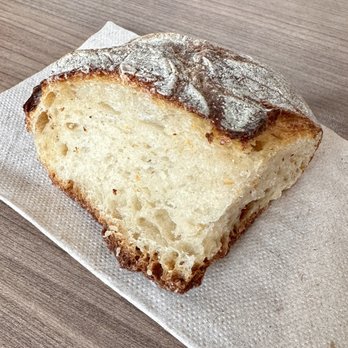 Pressed Cafe - Bread - A close-up image of a slice of rustic bread featuring a crusty, flour-dusted exterior and a soft, porous interior. The bread is positioned on a white paper napkin, resting on a wooden surface. The bread appears freshly baked with a golden-brown crust and an airy crumb structure. - Juice Bars & Smoothies Near Me - Newton, Massachusetts