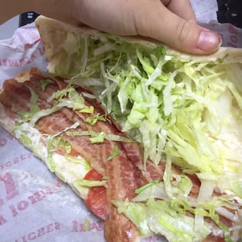 Jimmy John's - a hand holding a sandwich with lettuce and bacon - Fast Food Near Me - Springboro, Ohio