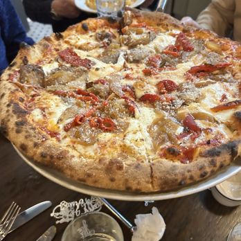 Bettola - A large pizza with cheese, red peppers, mushrooms, and meat toppings is on a table with drinks and utensils. - Pizza Near Me - Cranston, Rhode Island