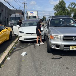 Just be careful with your Tesla's here. - A Tesla and a Nissan SUV are involved in a minor collision on a city street, with people inspecting the damage and debris on the road.