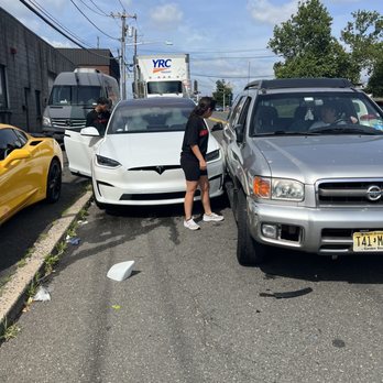 illmatic Wraps - Just be careful with your Tesla's here. - A Tesla and a Nissan SUV are involved in a minor collision on a city street, with people inspecting the damage and debris on the road. - Vehicle Wraps Near Me - Hackensack, New Jersey