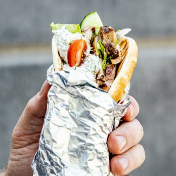 Halal Empire - a hand holding a sandwich wrapped in foil - Mediterranean Near Me Halal Empire - a hand holding a sandwich wrapped in foil - Mediterranean Near Me