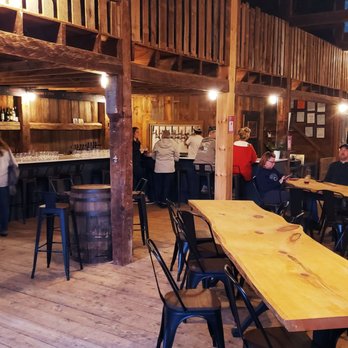Absolem Cider - Inside bar - A rustic cider house interior with wooden tables, chairs, and a bar area where patrons are seated and standing, with warm lighting. - Cideries Near Me - Winthrop, Maine