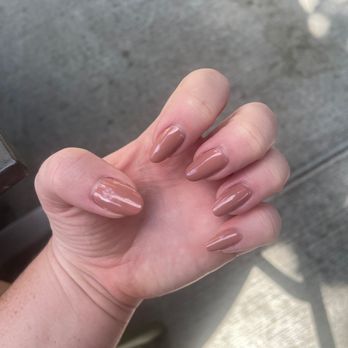 Tego Nail Spa - A close-up of a hand with neatly manicured nails painted in a nude shade, set against an outdoor background with concrete and a shadow. - Nail Salons Near Me - Chicago, Illinois
