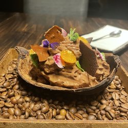 Nou Nikkei Cuisine - Chocolate mousse/ ice cream/ cake  served in a cacao pod on a bed of coffee beans and decorated with edible flowers and gooseberries.