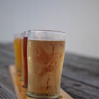 Arclight Brewing - Beer Flight - Four different beers in clear glasses are arranged on a wooden paddle, set on a rustic wooden table. - Breweries Near Me - Watervliet, Michigan