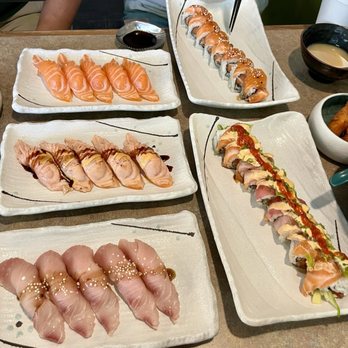 Sushibucks - A variety of sushi rolls and sashimi are presented on rectangular ceramic plates, with soy sauce and dipping sauces nearby, in a restaurant setting. - Japanese Near Me - Albuquerque, New Mexico