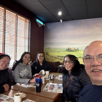 Riverside Diner - Five people are seated at a restaurant table, smiling and posing for a selfie with a scenic mural in the background. - Diners Near Me - Belvidere, New Jersey
