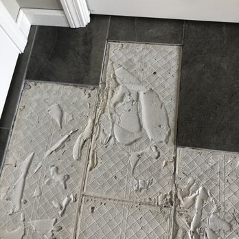 Costa's Masonry - a close up of a tile floor - Damaged tile floor with broken tiles and uneven grout near a door, showing signs of wear or repair work. - Stonemasons Near Me - Methuen, Massachusetts