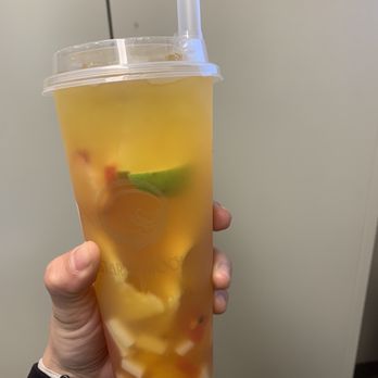 Starry Moon - Passion fruit tea with rainbow jellies - A person holds a large, transparent cup filled with passion fruit tea that contains rainbow-colored jellies, slices of lime, and other fruit pieces. The cup has a plastic lid with a straw inserted. The background is plain and neutral, emphasizing the beverage's colorful contents. - Bubble Tea Near Me - Albuquerque, New Mexico