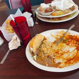 two plates of food on a table - A plate with remnants of Mexican food, including a taco and sauce, on a dark wooden table with drinks, chips, and condiments.