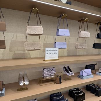 Tory Burch - A retail display features handbags, shoes, and accessories arranged on wooden shelves with a promotional sign. - Fashion Near Me - Central Valley, New York
