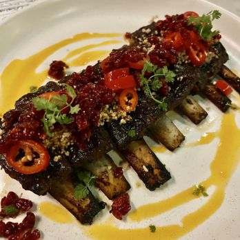 Eyval - Lamb ribs - Lamb ribs are served with chili slices, herbs, and a sauce, presented on a white plate in a restaurant setting. - Persian/Iranian Near Me - Brooklyn, New York