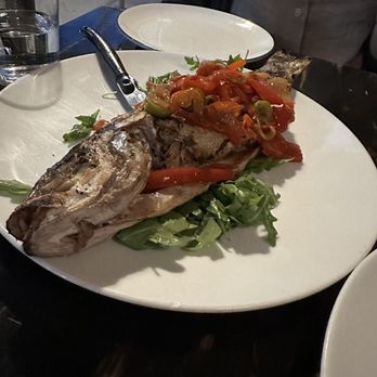 Bar Volpe - Pesce alla Griglia - A whole grilled fish with a tomato and vegetable sauce, garnished with greens, on a white plate at a restaurant. - Italian Near Me - Boston, Massachusetts