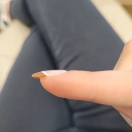 A person's finger with a long, pointed, natural-looking nail is shown, with the background blurred and the person wearing dark clothing.