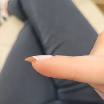 Gorgeous Nails - A person's finger with a long, pointed, natural-looking nail is shown, with the background blurred and the person wearing dark clothing. - Nail Salons Near Me - Modesto, California